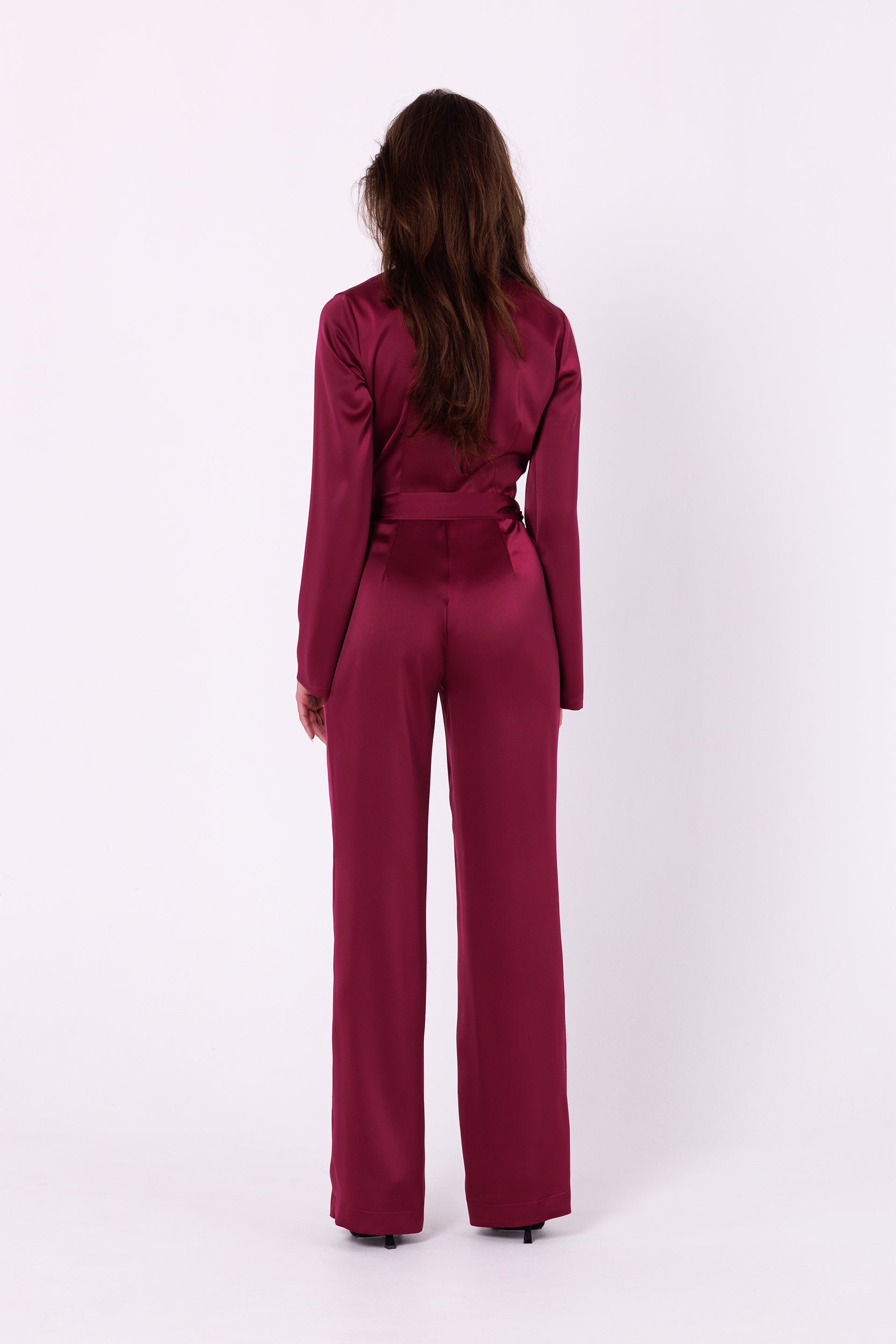 Long Sleeve Wine Red Satin Jumpsuit | Strictly In | Make a statement at your next event with our Long Sleeve Satin Jumpsuit. Crafted from luxurious satin, it features a V-neck, long sleeves, and a tied waist for a glamorous yet comfortable look. Perfect for the party season.