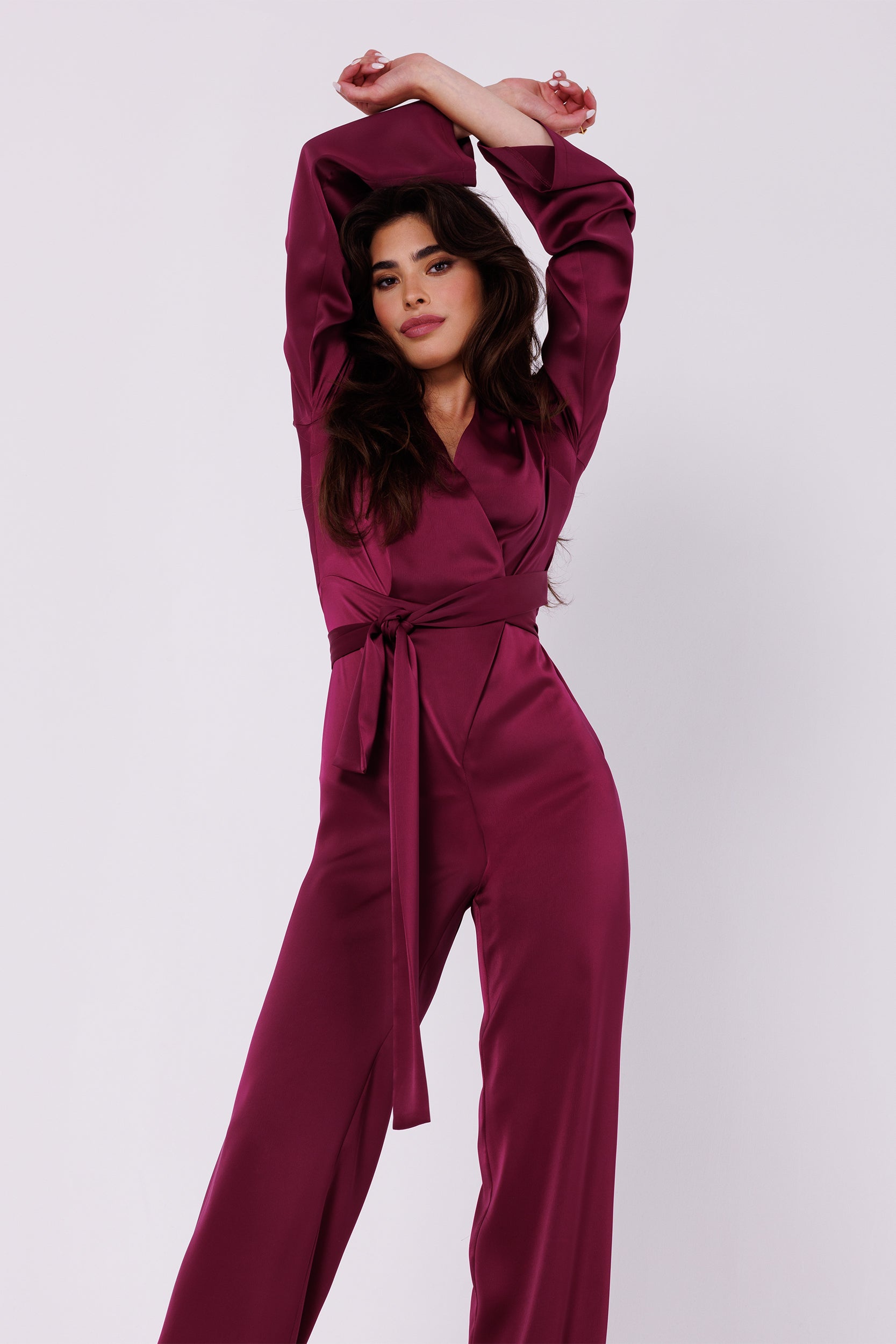 Long Sleeve Wine Red Satin Jumpsuit | Strictly In | Make a statement at your next event with our Long Sleeve Satin Jumpsuit. Crafted from luxurious satin, it features a V-neck, long sleeves, and a tied waist for a glamorous yet comfortable look. Perfect for the party season.