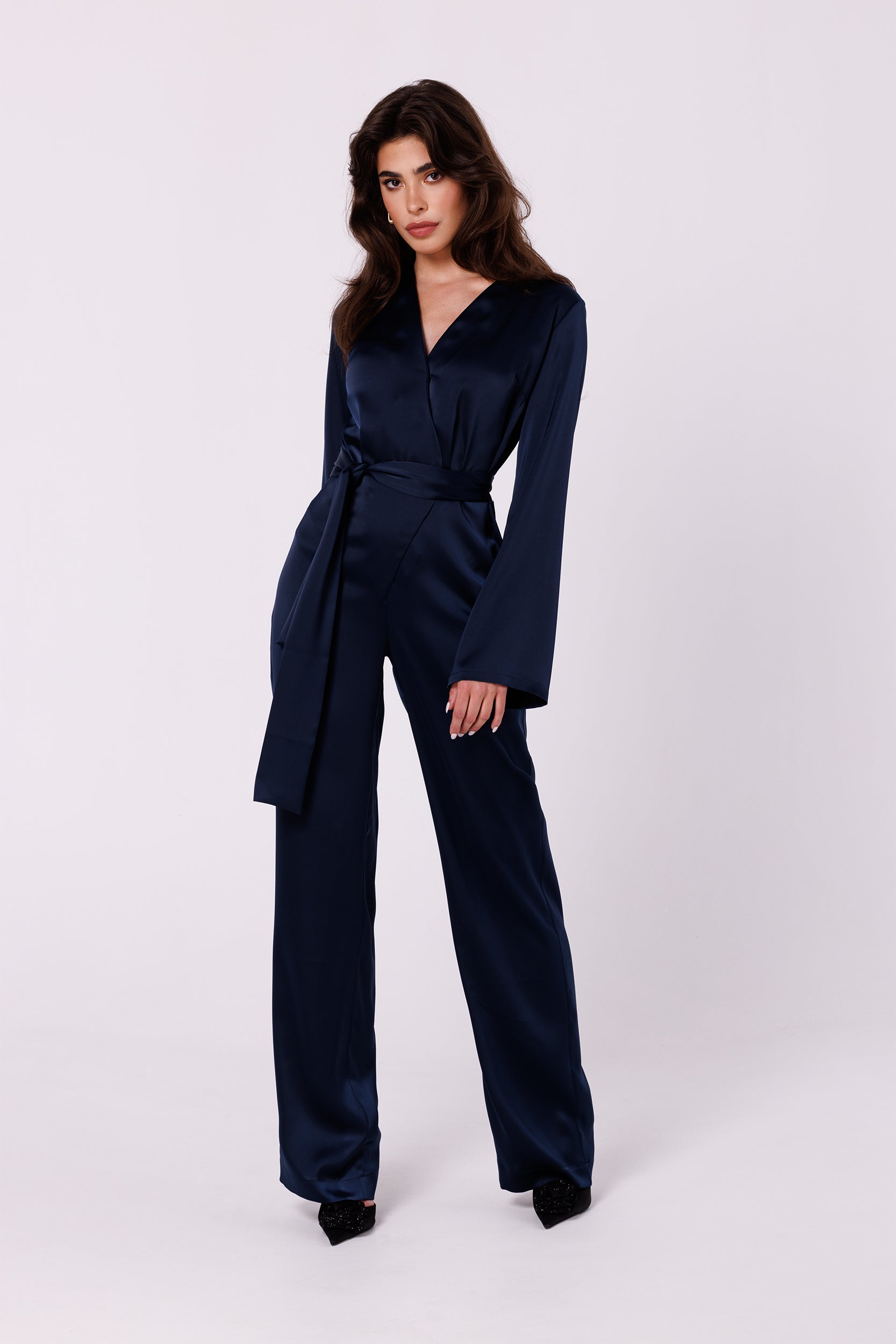 Long Sleeve Night Blue Satin Jumpsuit | Strictly In | Make a statement at your next event with our Long Sleeve Satin Jumpsuit. Crafted from luxurious satin, it features a V-neck, long sleeves, and a tied waist for a glamorous yet comfortable look. Perfect for the party season.